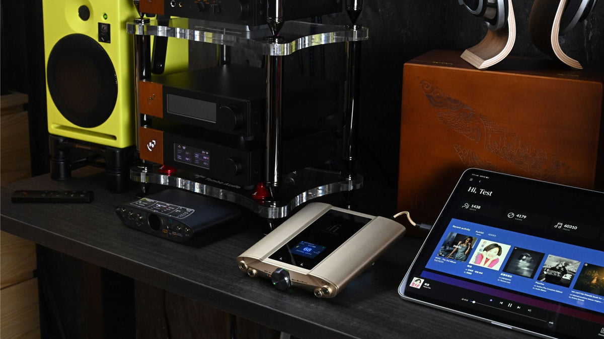 Audio equipment on a desk with a tablet displaying music app.